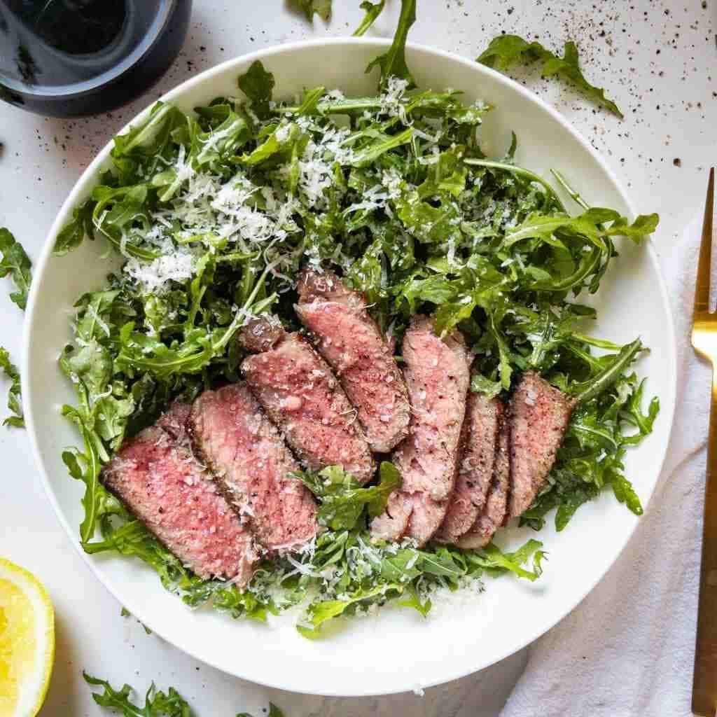 sliced steak served over a bed of fresh arugula with grated parmesan cheese.