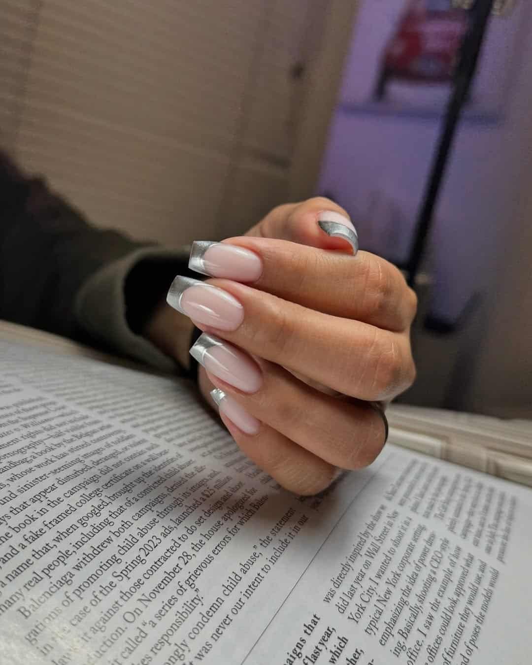 nude fingernails with silver tips held over newspaper