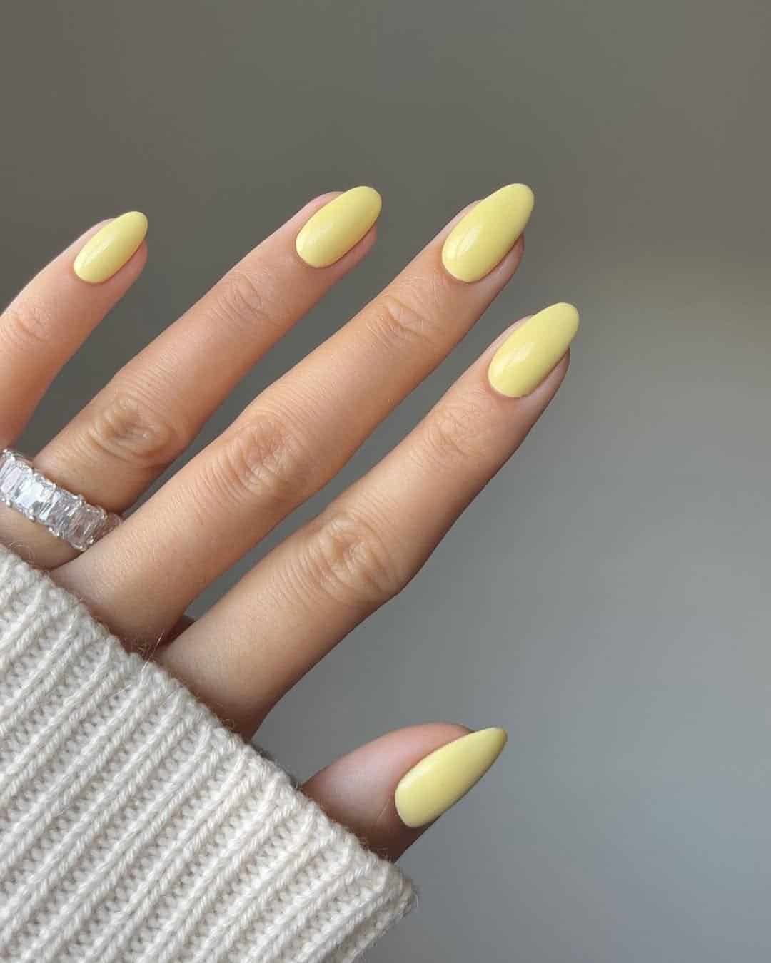 solid pale yellow almond shaped nails with a silver ring and sweater cuff