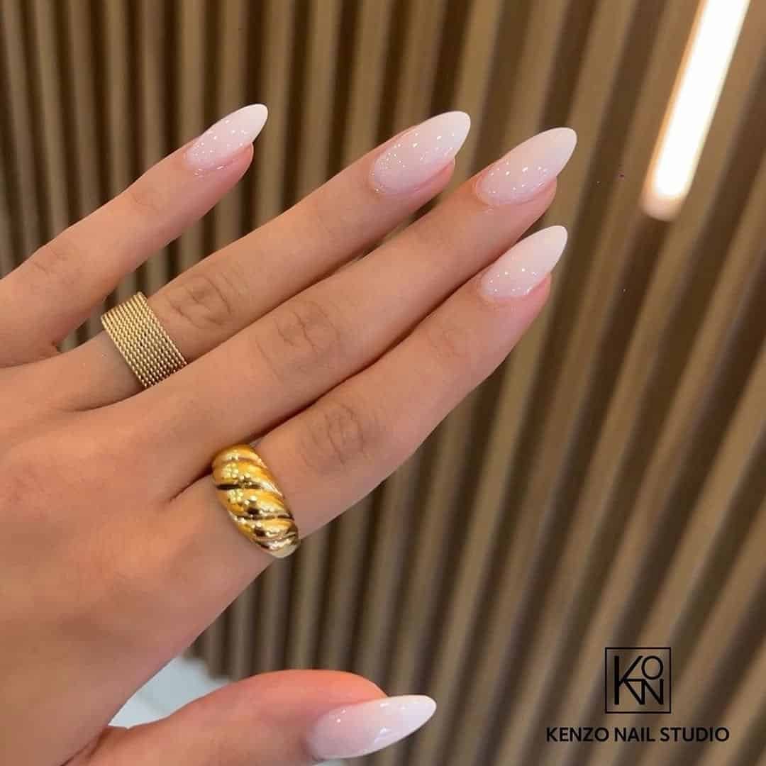 milky white almond nails featuring two gold rings on the hand