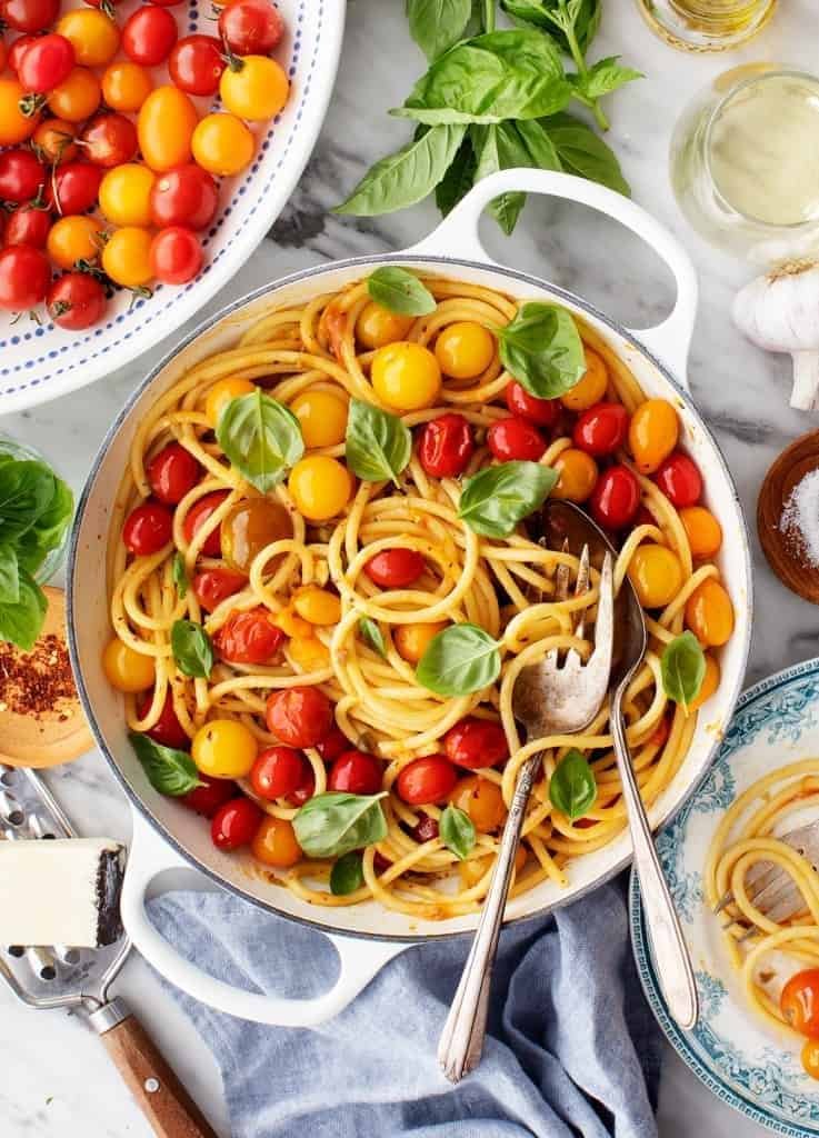spaghetti with colorful roasted cherry tomatoes and fresh basil leaves in a white skillet.