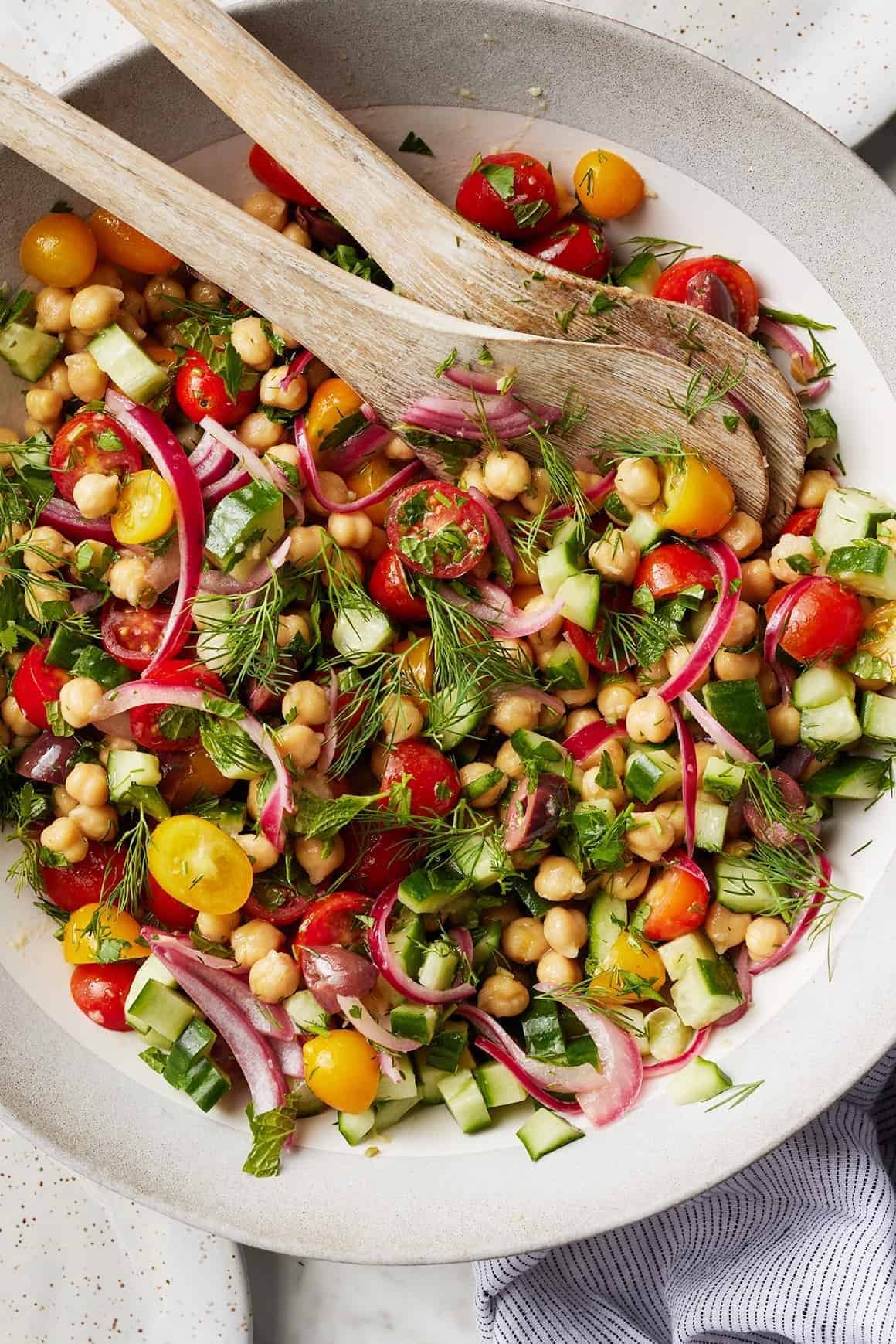 colorful chickpea salad with cucumbers, red onions, tomatoes, and fresh herbs in a white bowl.