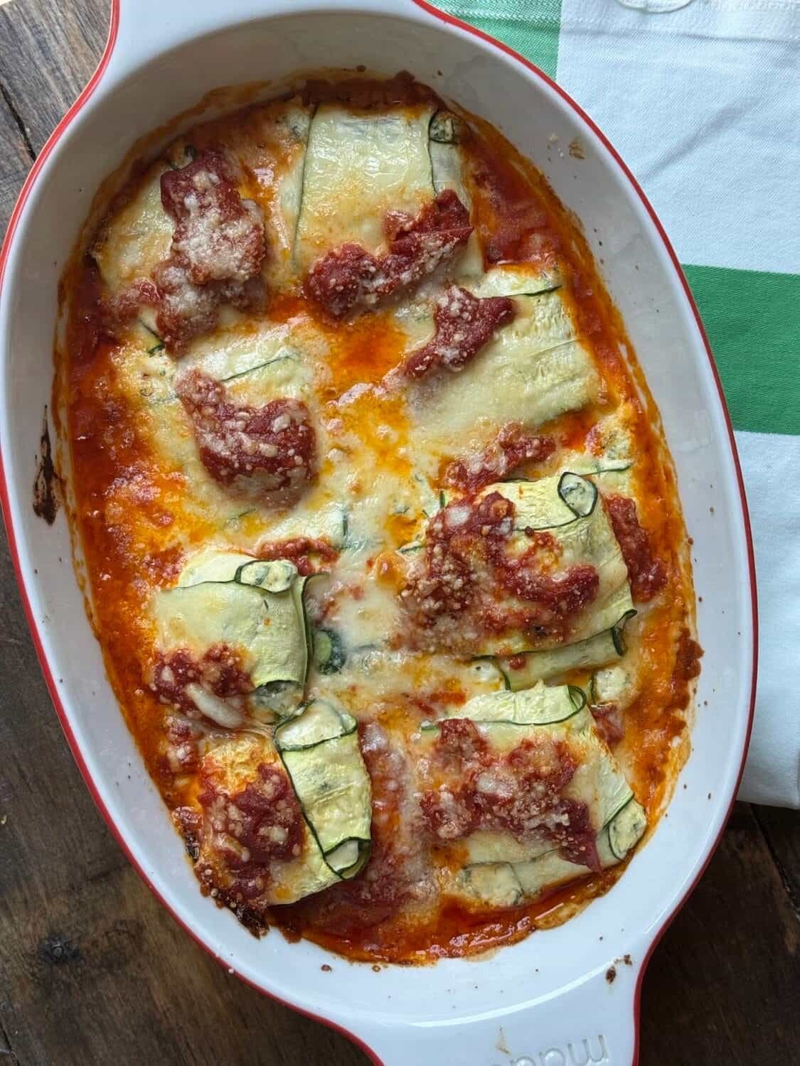 baked zucchini ravioli rolls topped with tomato sauce and melted cheese in a casserole dish.