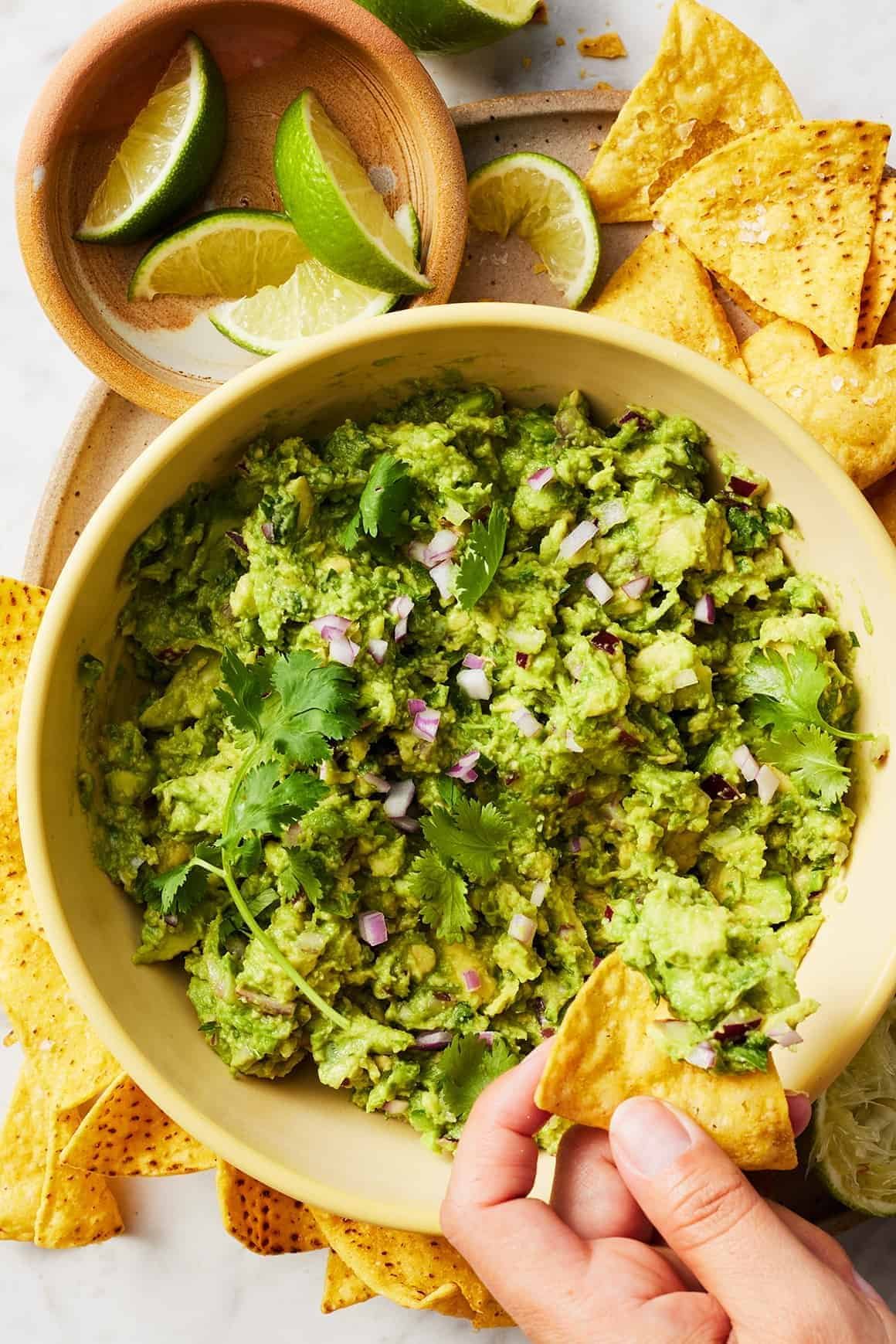 fresh guacamole in a bowl with red onion, cilantro, and lime wedges