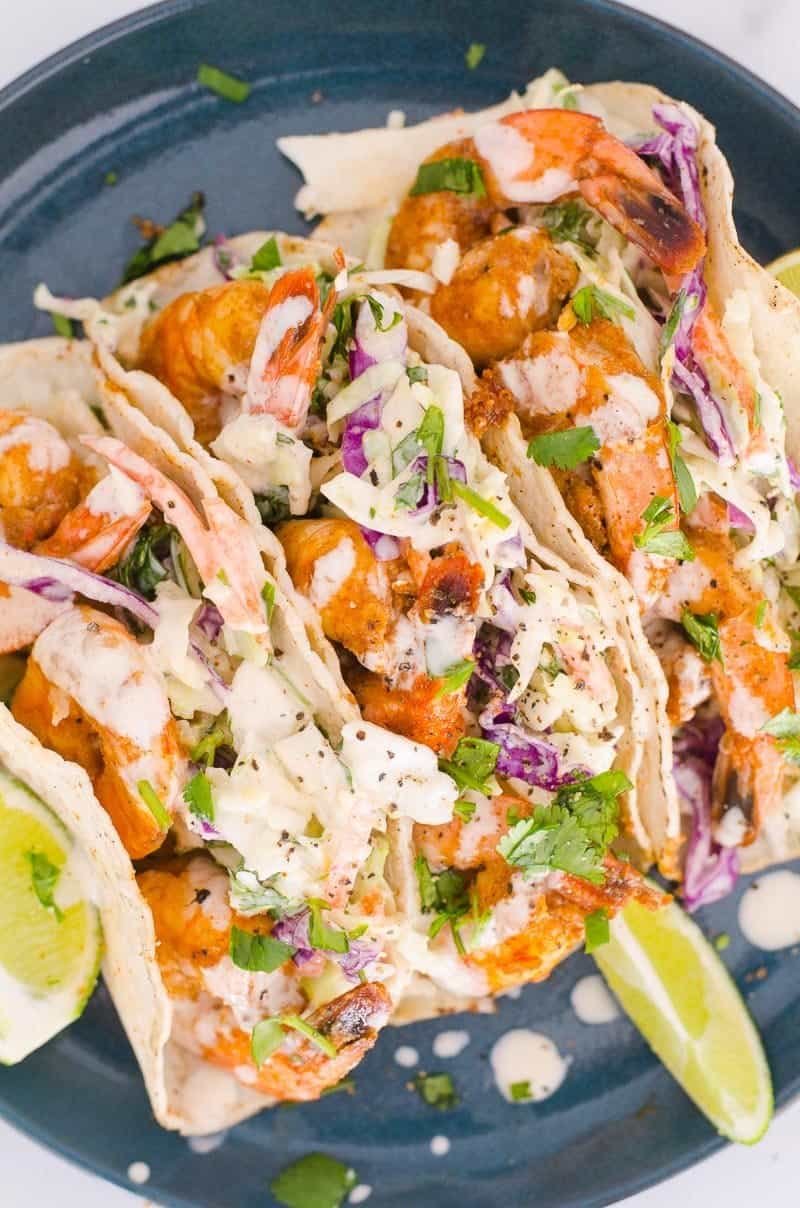 shrimp tacos with colorful cabbage slaw and creamy sauce on a dark blue plate.