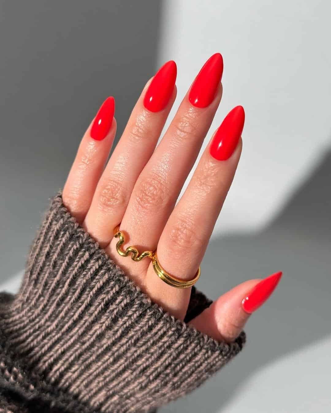 long almond nails in a vibrant glossy solid red with gold rings.