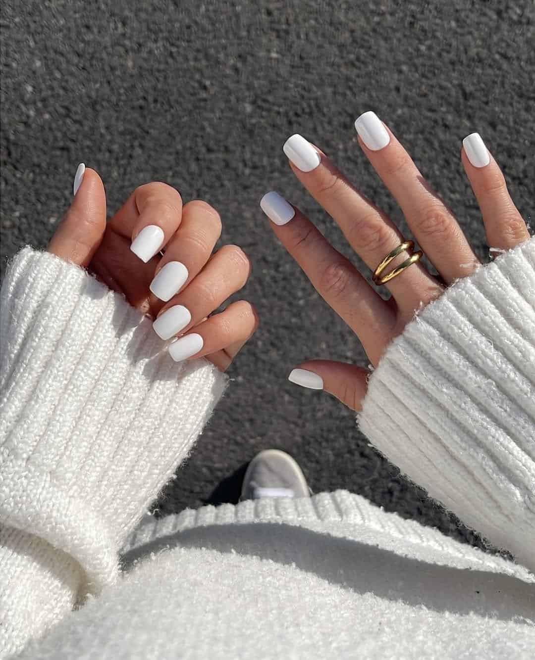 square white nails on hands wearing a white knit sweater and gold rings.
