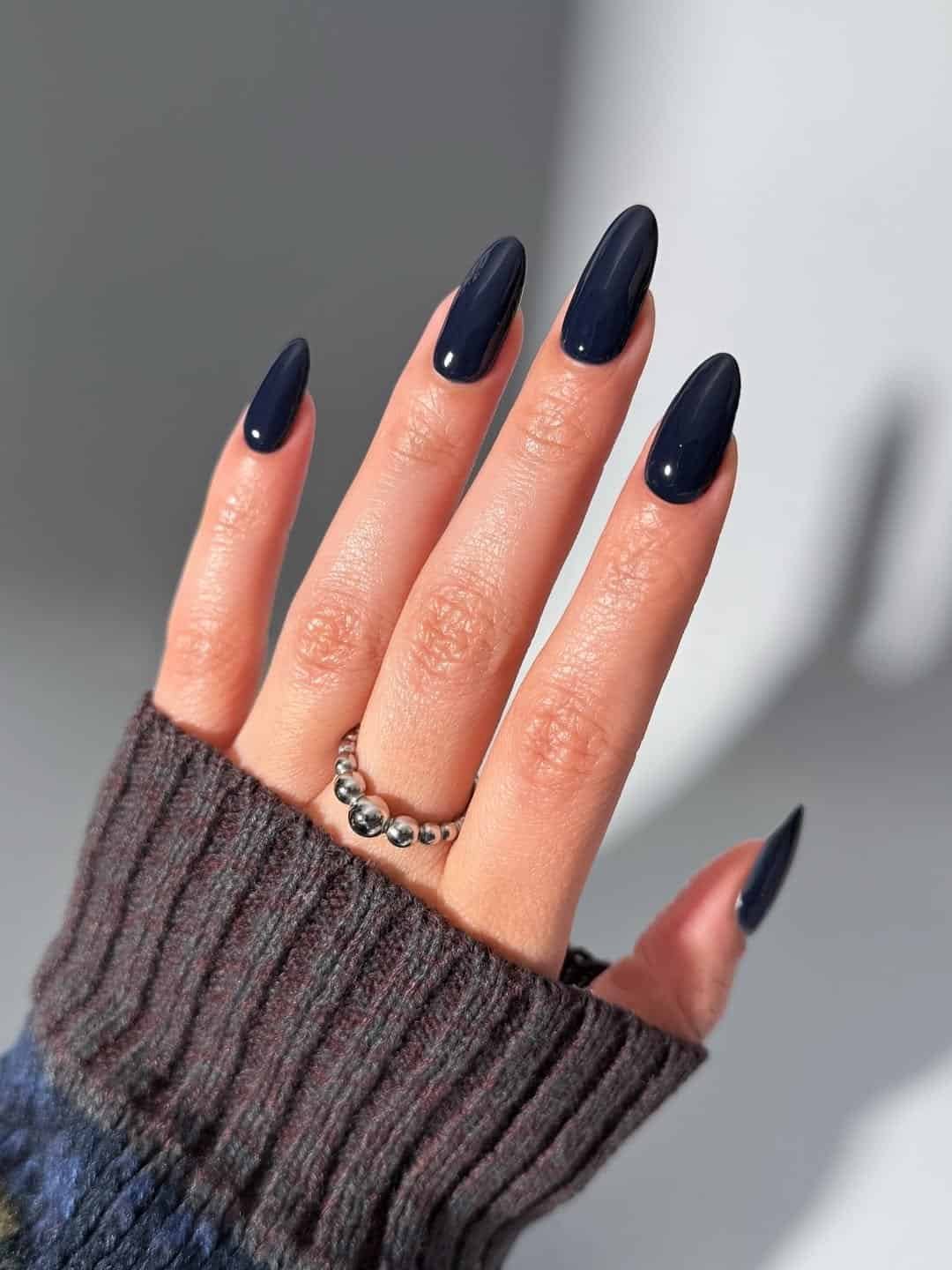 long almond nails in a solid glossy navy blue with a silver ring.