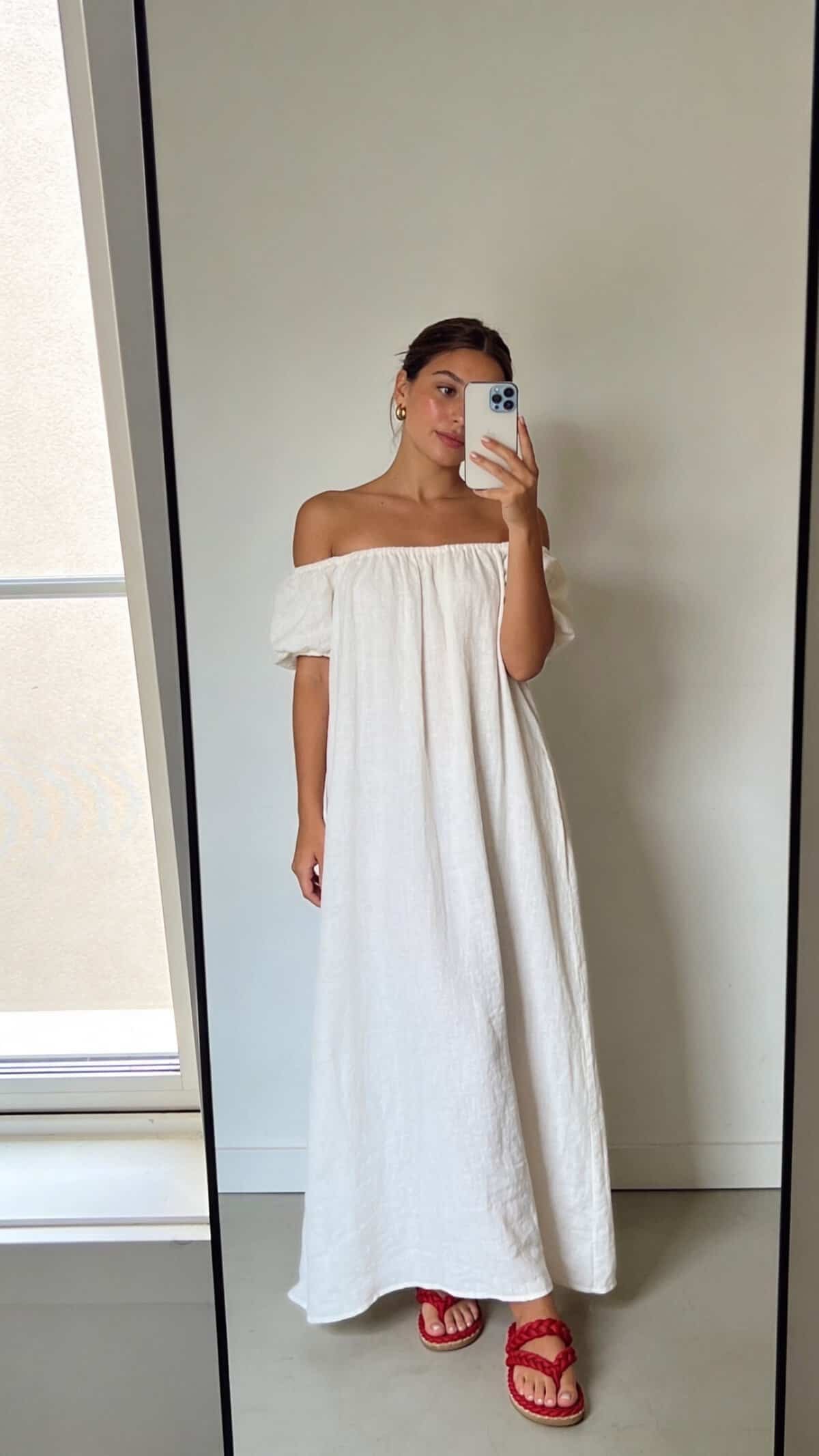 woman wearing off-the-shoulder white maxi dress with red braided sandals.