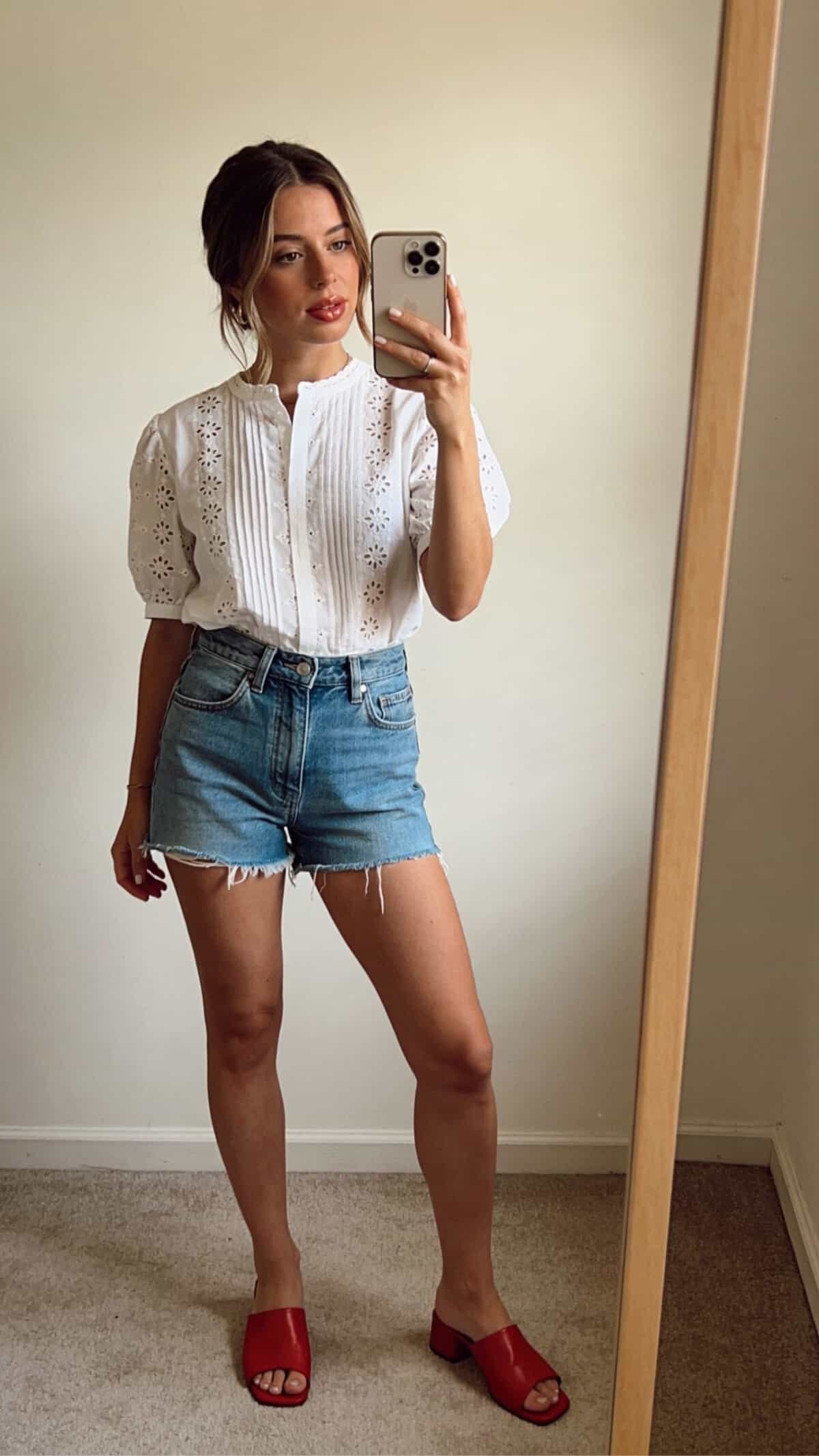 woman wearing white eyelet blouse and denim shorts with red mule sandals.