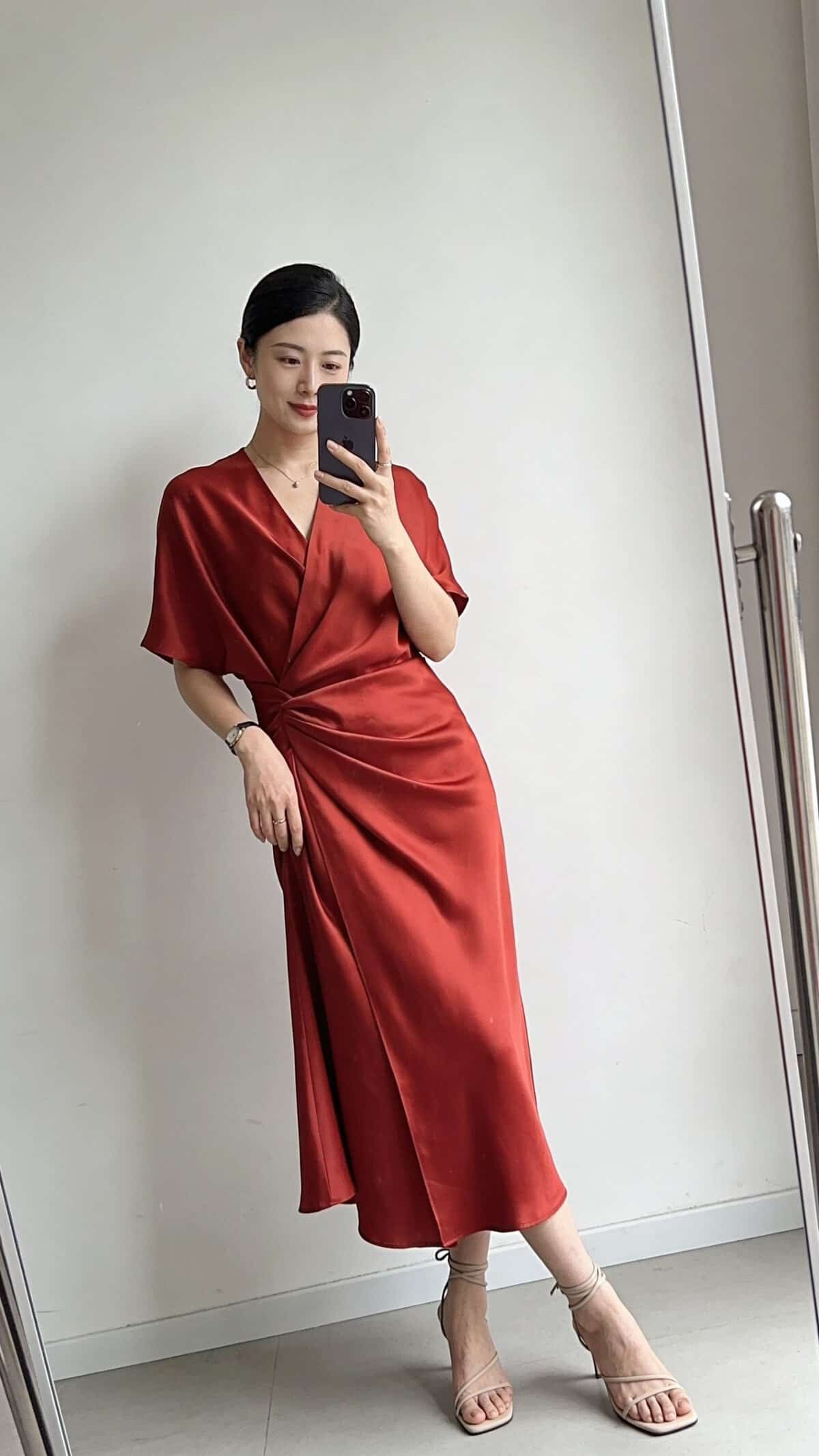woman in red wrap dress and strappy heels taking a mirror selfie.