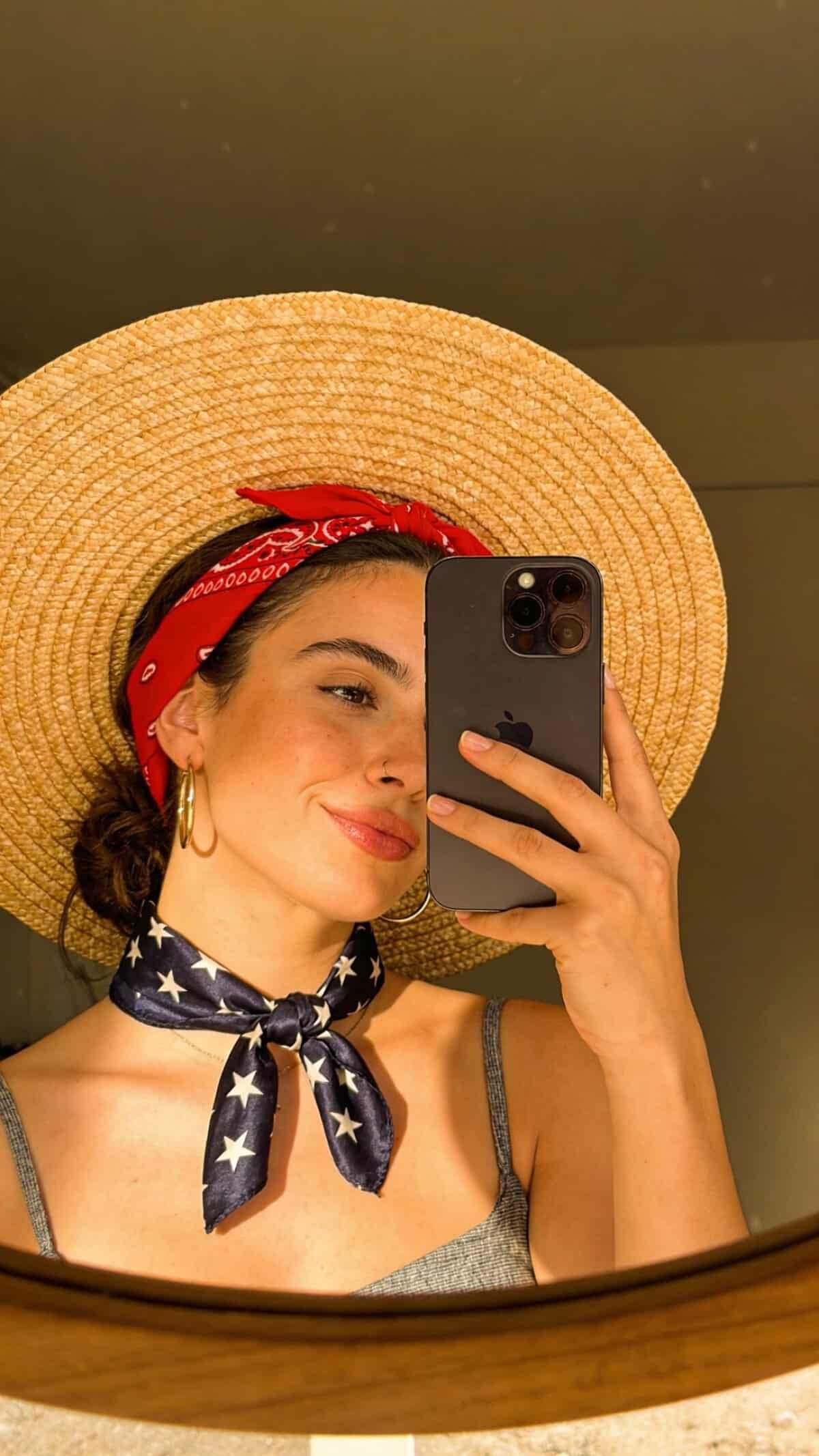 woman with straw hat, red bandana, and star patterned neck scarf smiling.