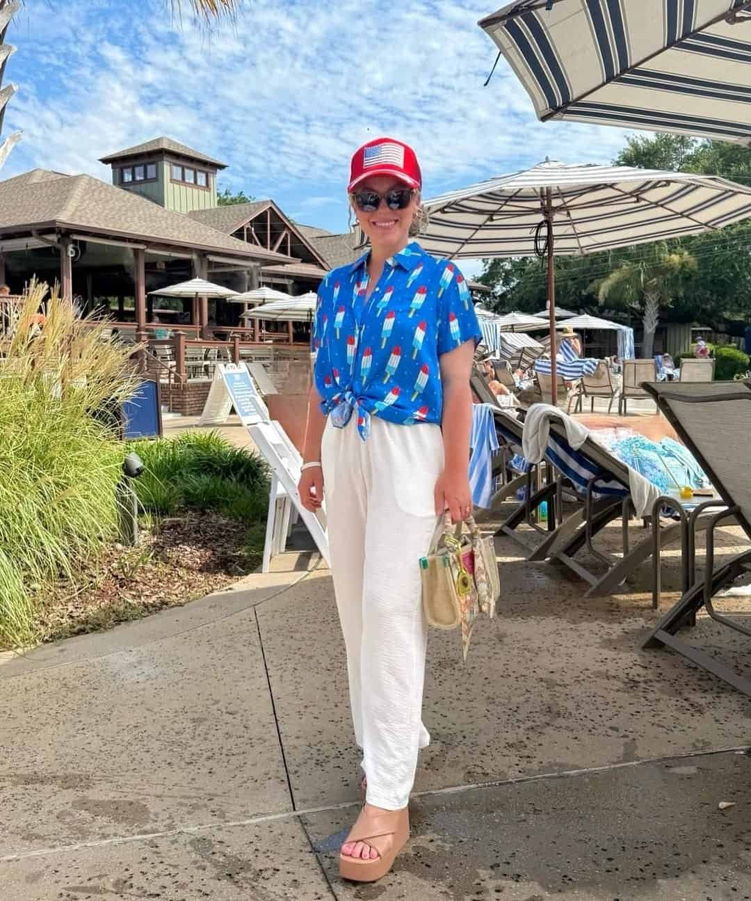 woman wearing popsicle print shirt and red american flag hat at outdoor resort.
