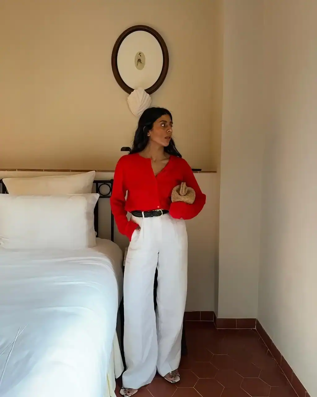 woman wearing red button-down shirt and white wide-leg trousers holding straw clutch.