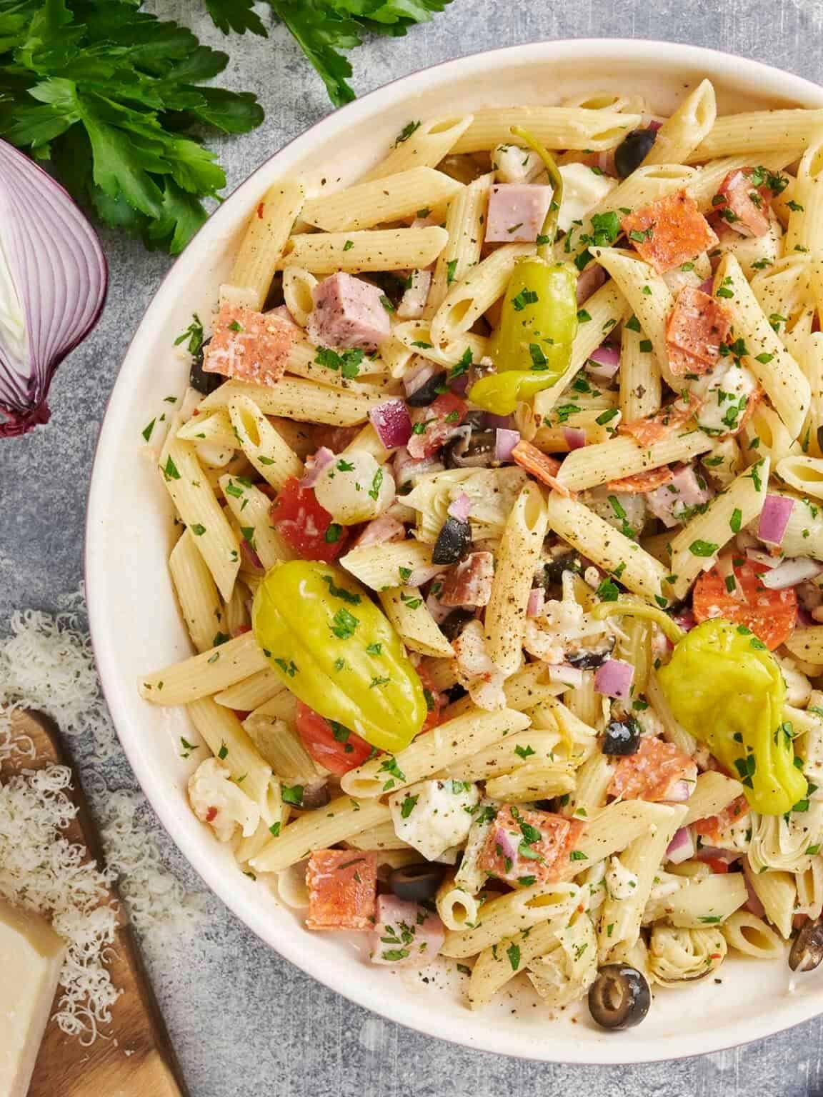 bowl of antipasto pasta salad with penne, salami, red onion, and whole pepperoncini peppers