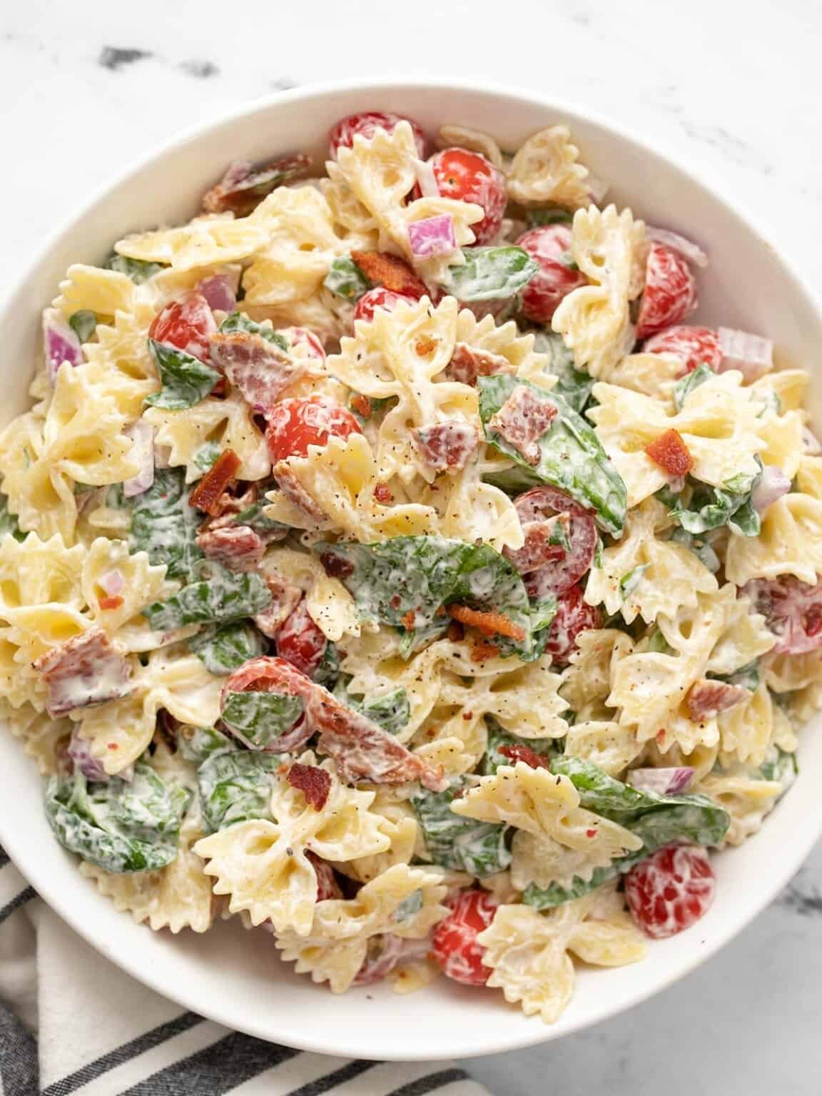 bow tie pasta salad with tomatoes, spinach, and bacon bits in a creamy dressing