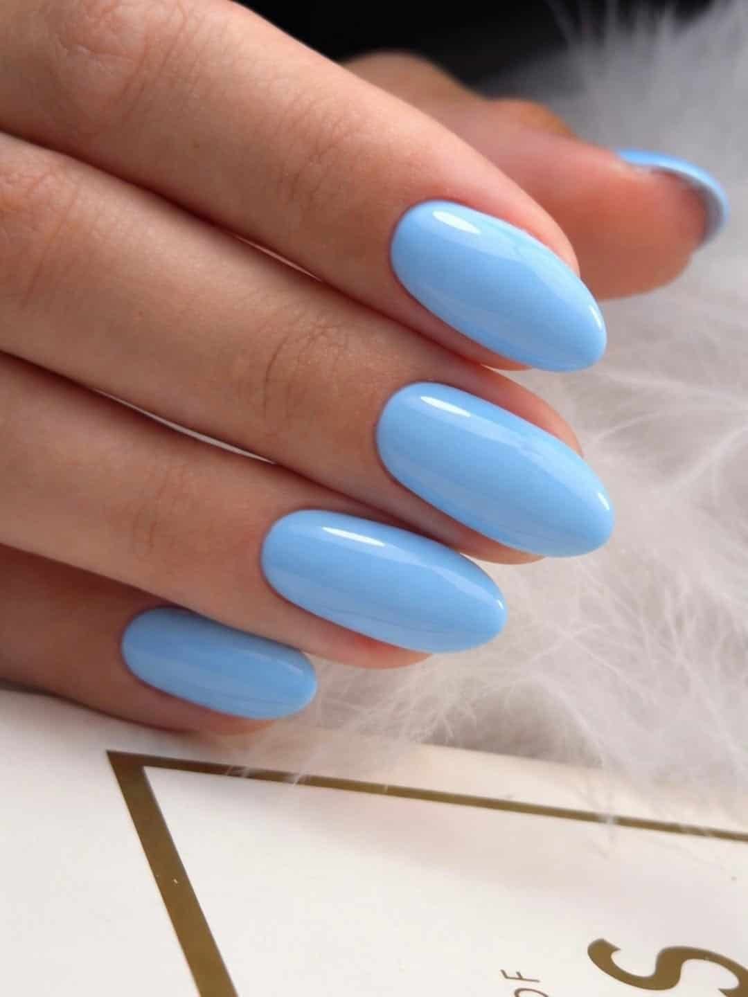 glossy pastel light blue oval manicure shown resting against a soft white feather background