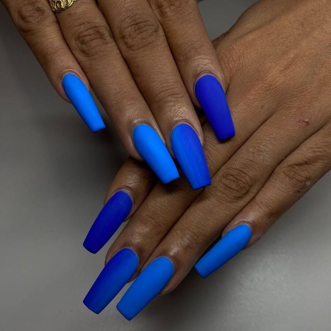 long coffin shaped nails with a matte finish in alternating shades of royal blue