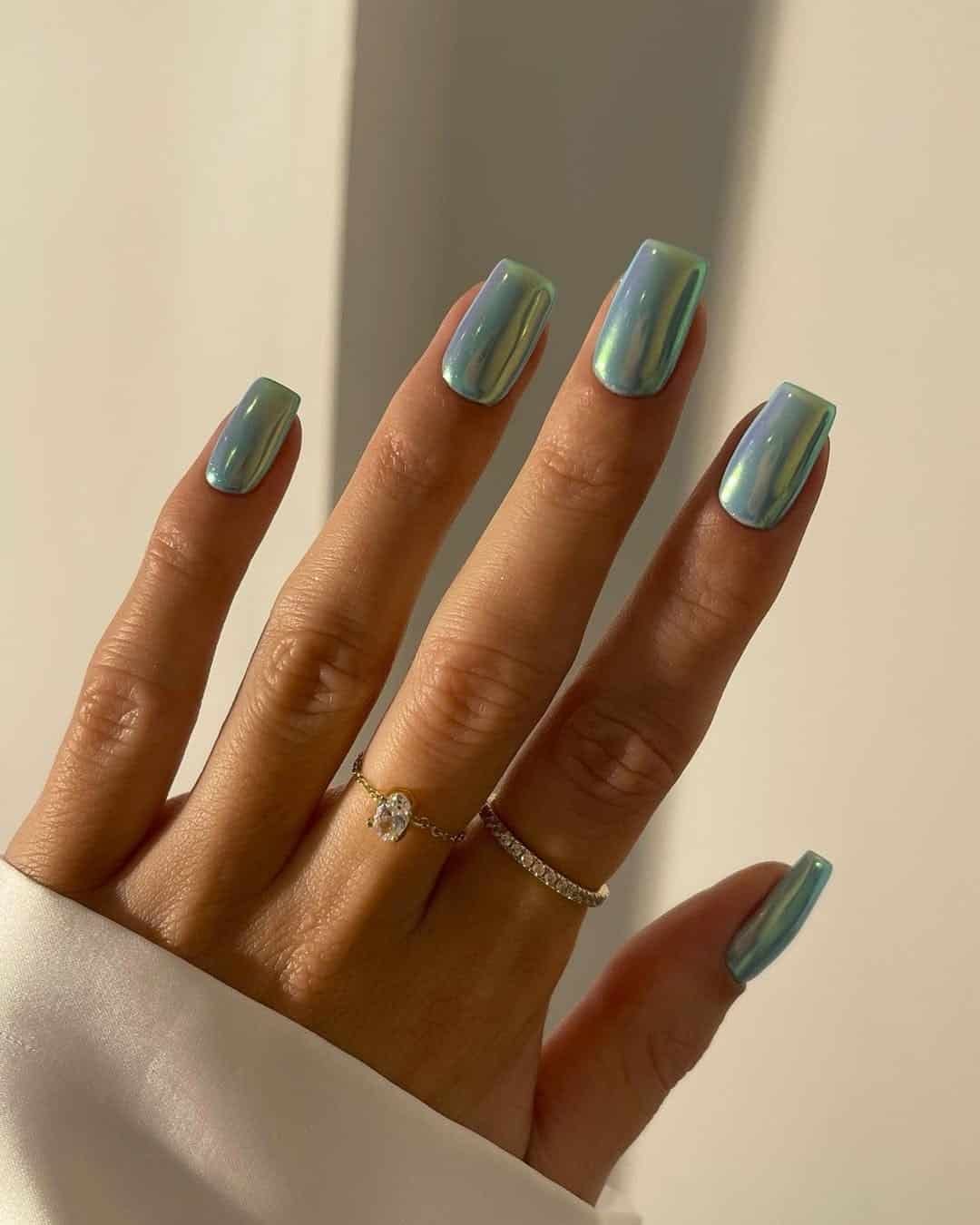 long square nails with a shiny iridescent blue chrome finish and simple gold rings