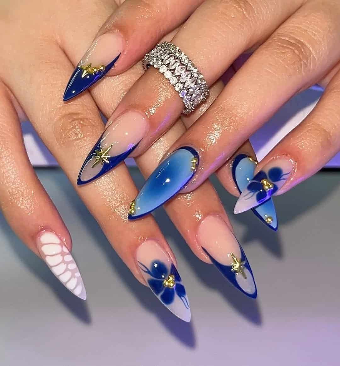 long stiletto nails with dark blue french tips, floral art, and gold star accents