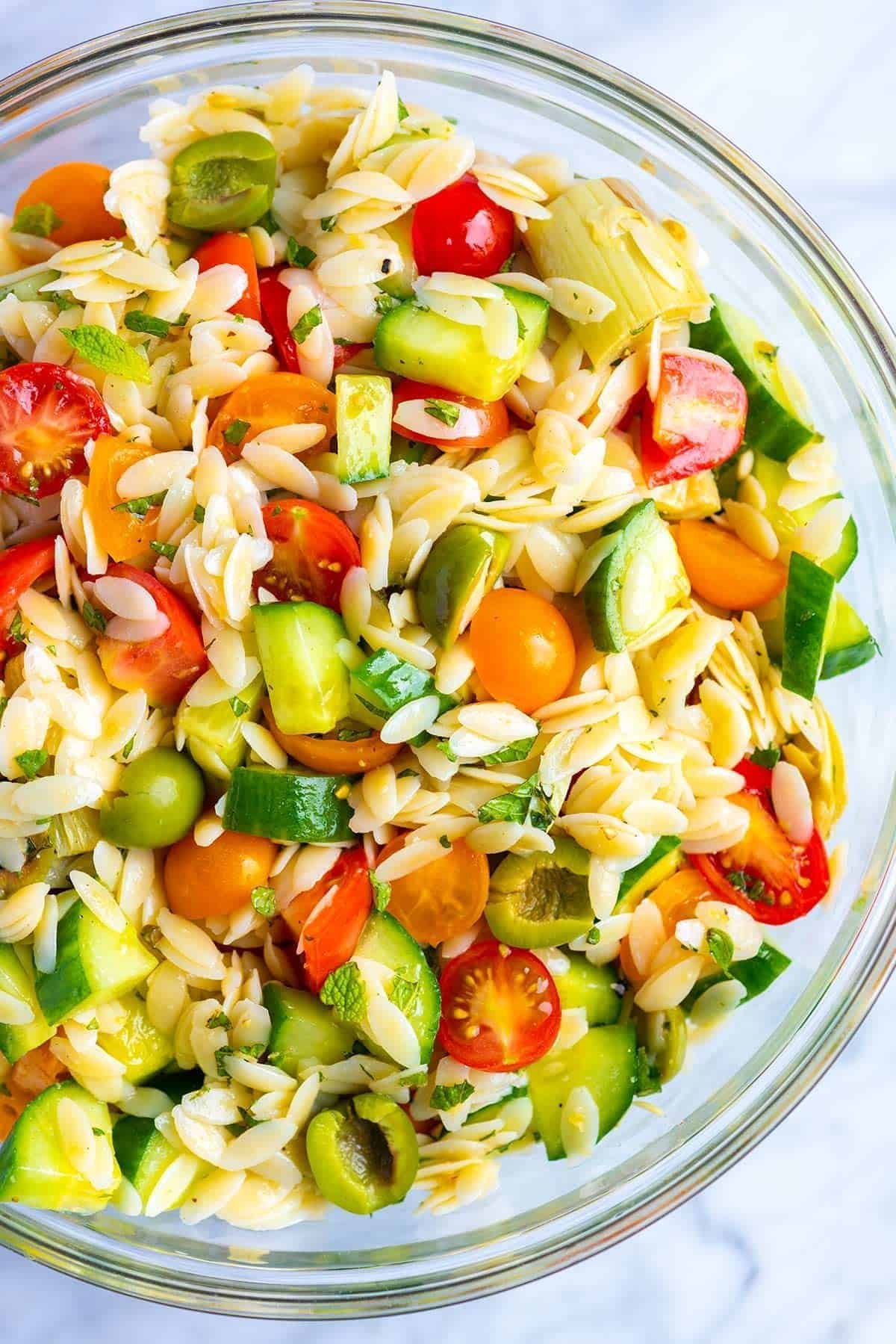 glass bowl of orzo pasta salad with halved cherry tomatoes, cucumbers, and green olives
