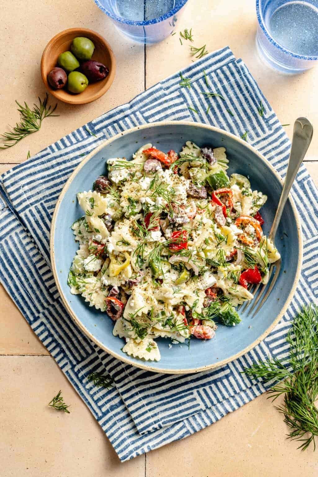 bow tie pasta salad with feta, olives, and bell peppers on a striped napkin