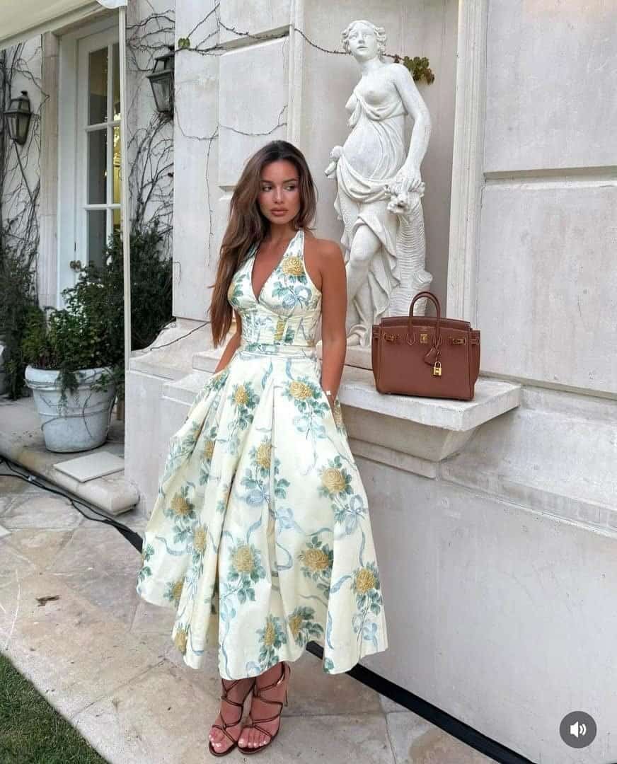 woman posing outdoors in an ivory halter midi dress with green floral patterns