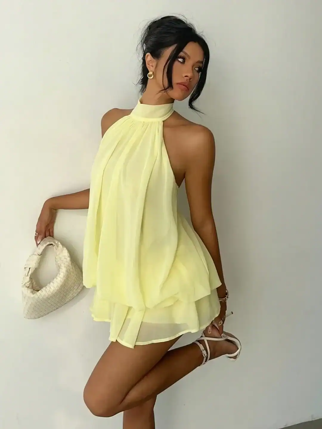 woman in a pale yellow halter neck chiffon mini dress holding a woven bag
