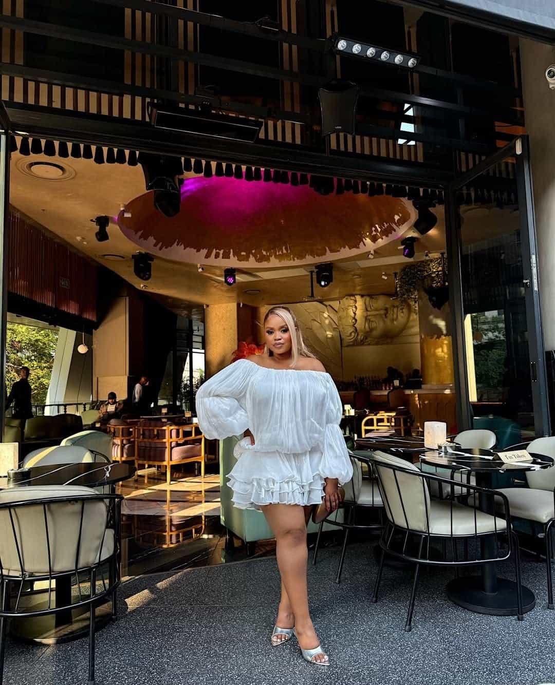 woman posing at an outdoor restaurant wearing a white off the shoulder ruffle dress