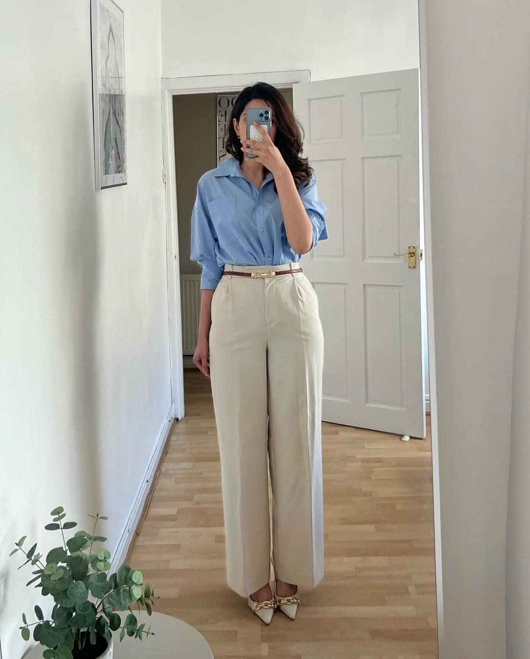 woman posing in blue button down shirt tucked into cream high waisted trousers