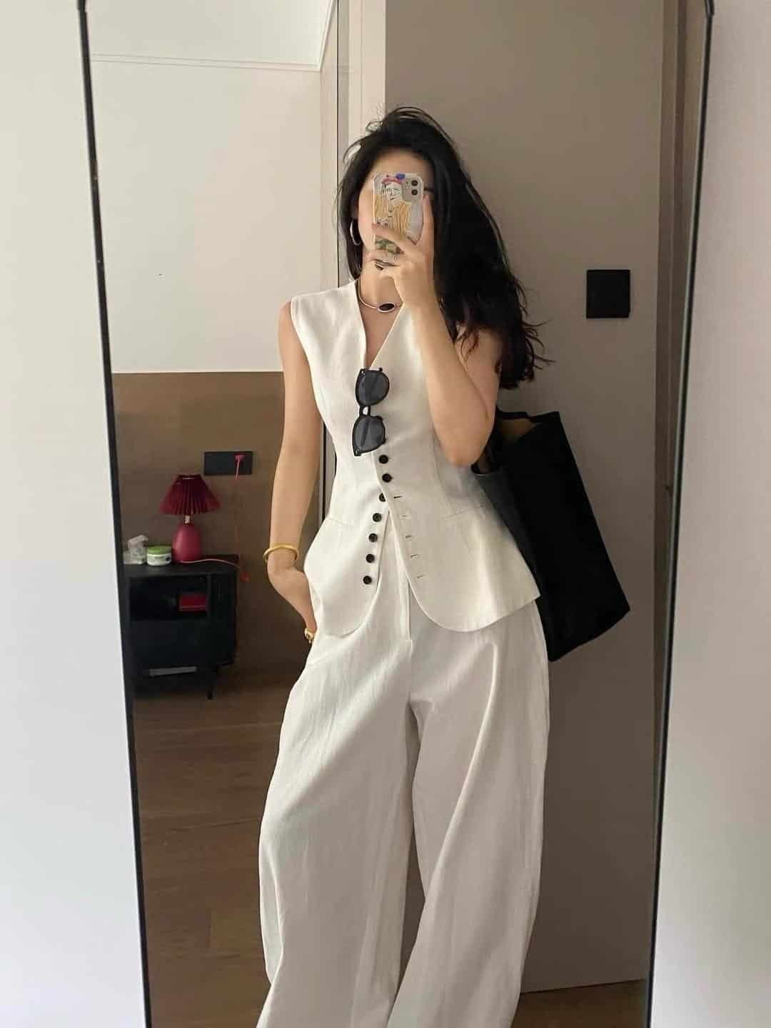 woman taking a mirror selfie wearing white sleeveless vest and matching wide leg trousers