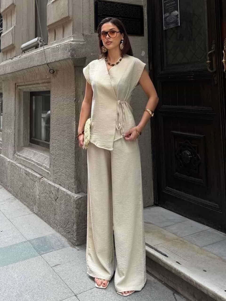 woman wearing sleeveless beige wrap top and matching wide leg trousers on city sidewalk