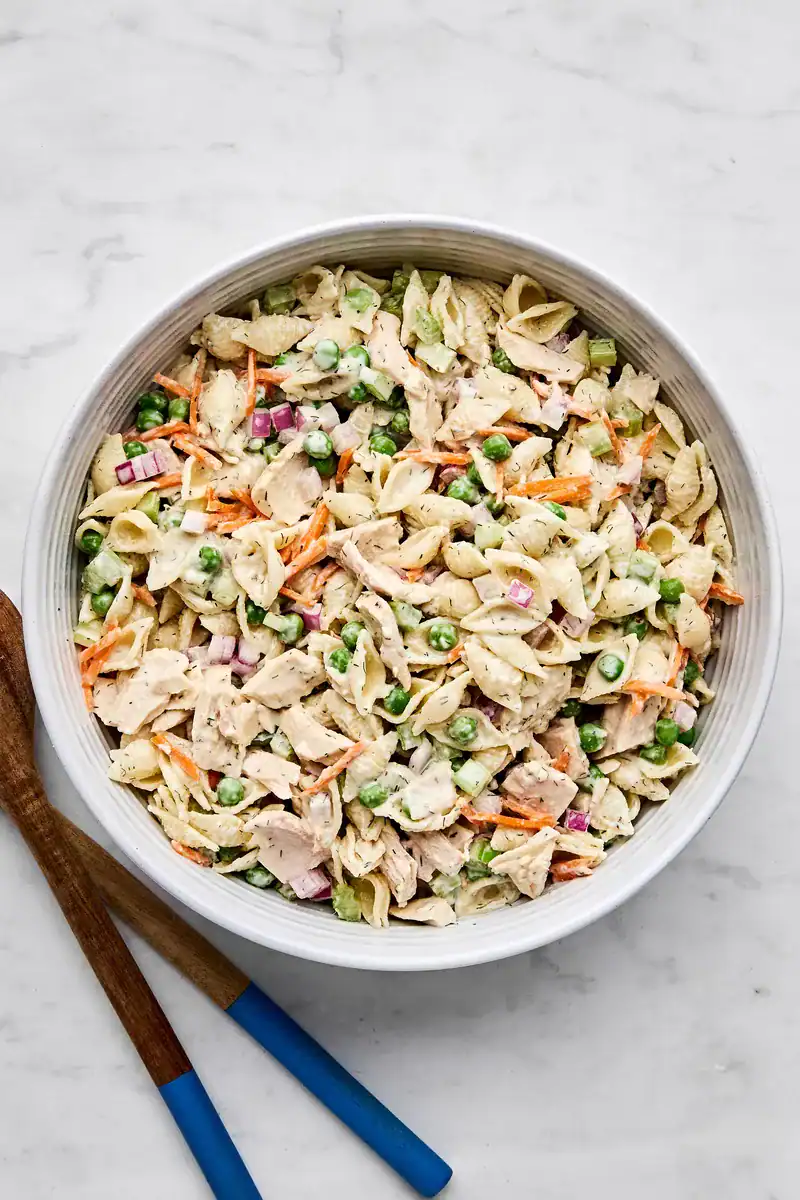 creamy shell pasta salad with tuna, peas, carrots, and red onions in a bowl
