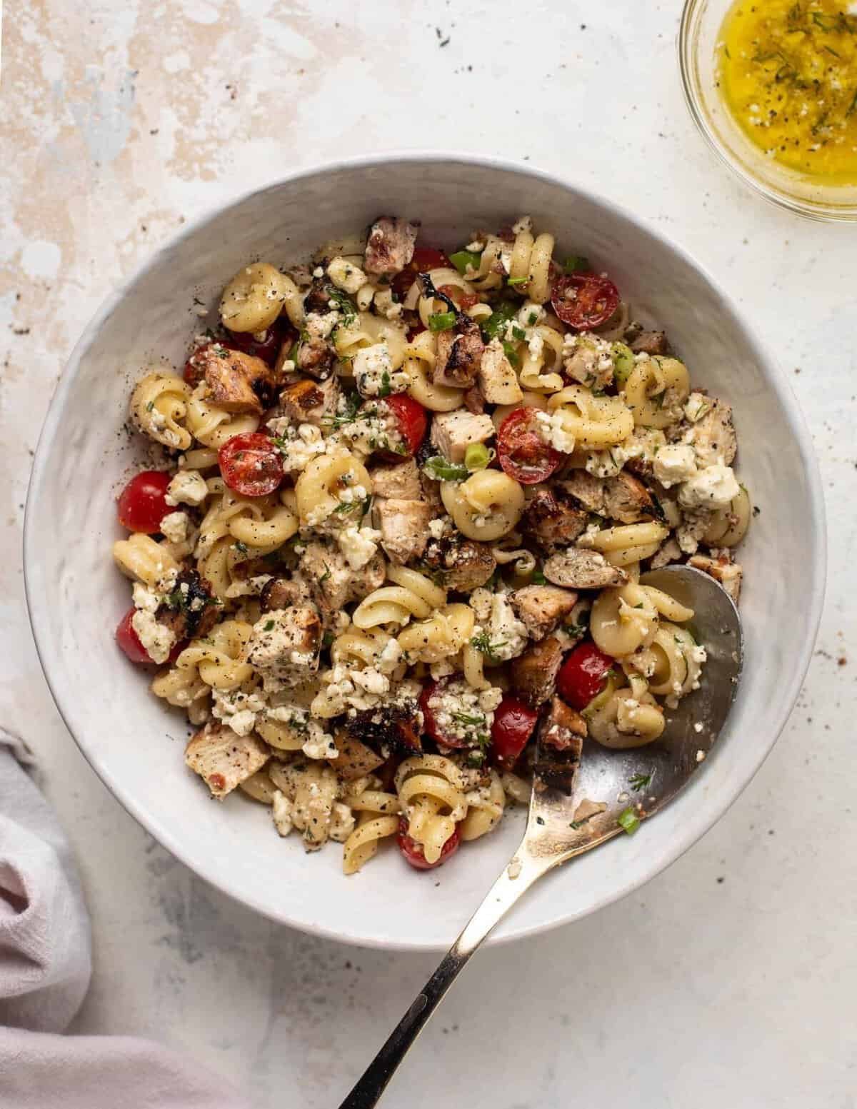 grilled chicken pasta salad with cherry tomatoes and feta cheese in a white bowl