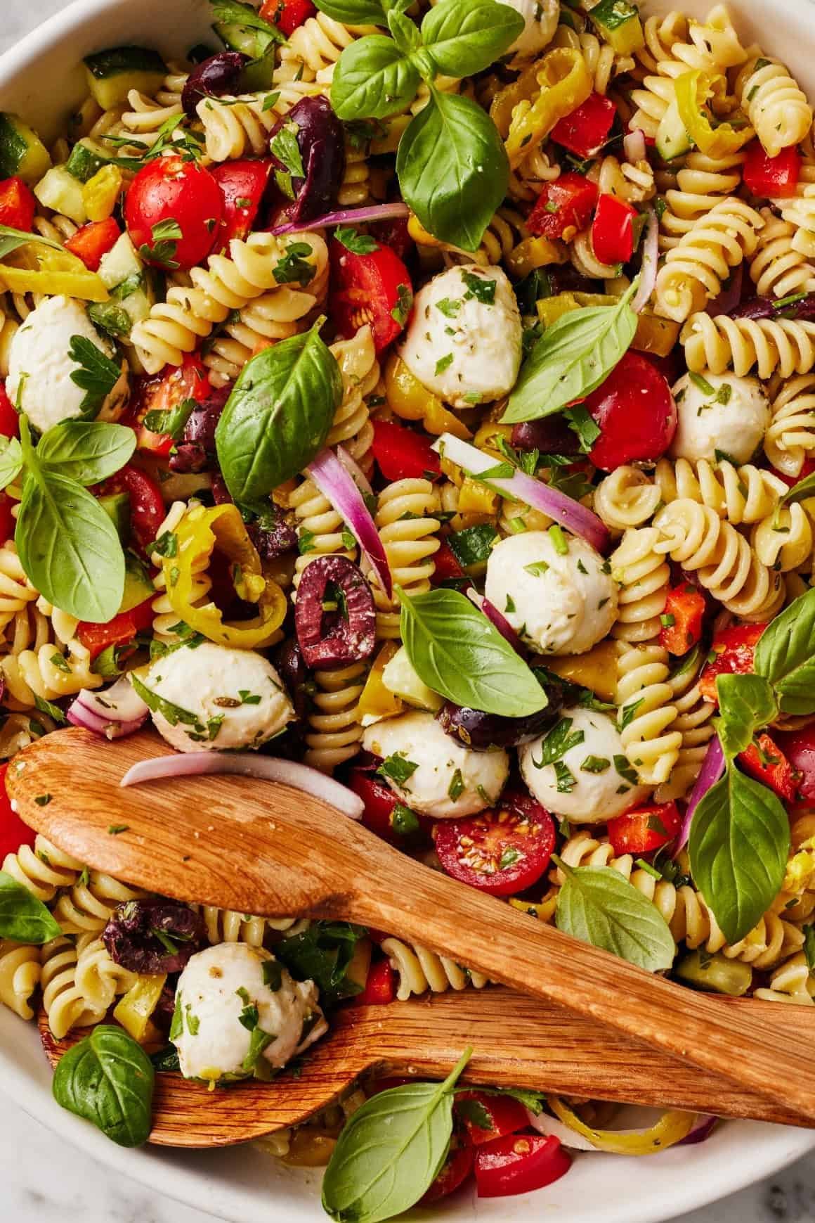 italian pasta salad with rotini, mozzarella balls, olives, tomatoes, and fresh basil leaves