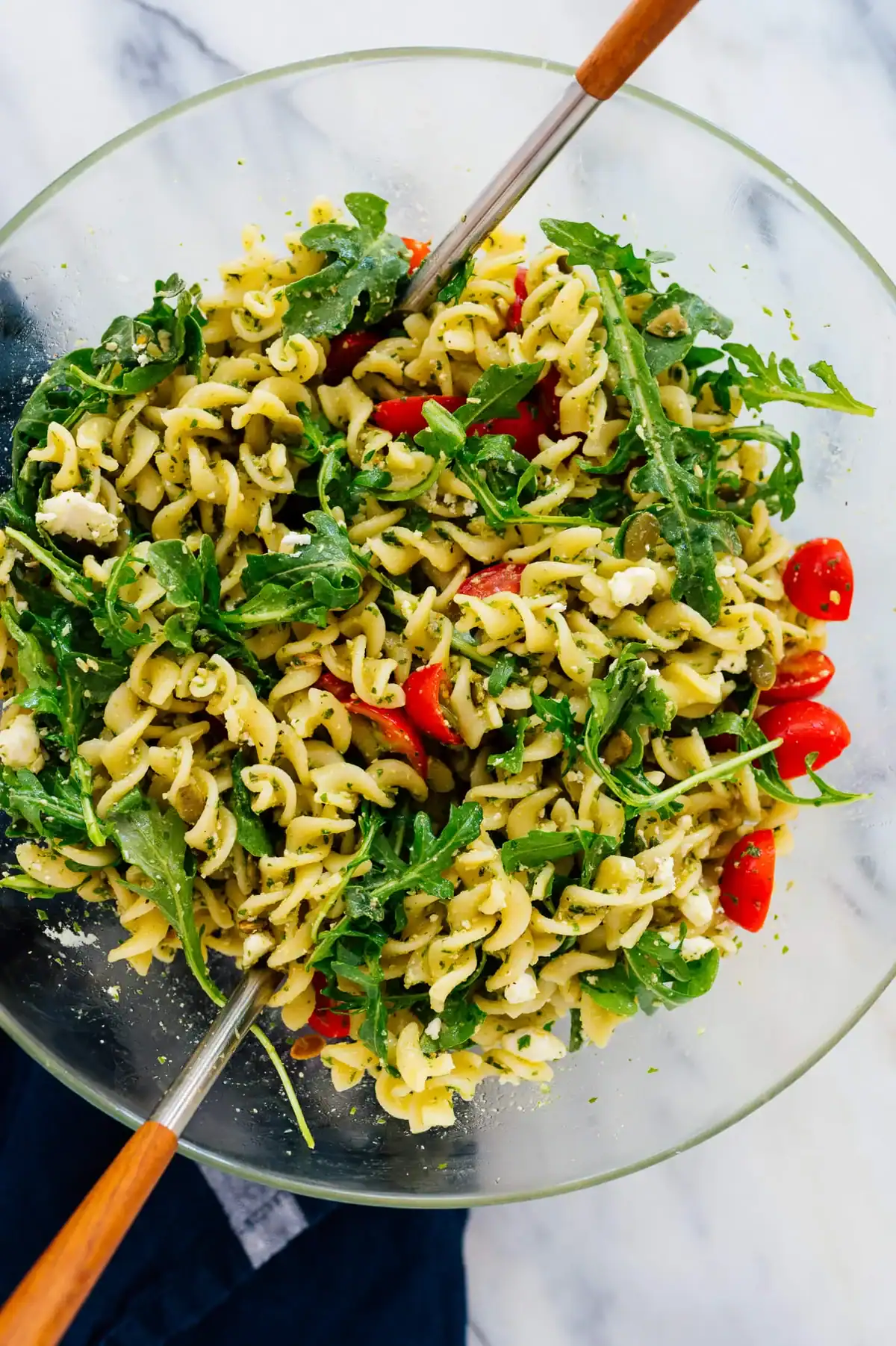 glass bowl of pesto pasta salad with fusilli, fresh arugula, and cherry tomatoes