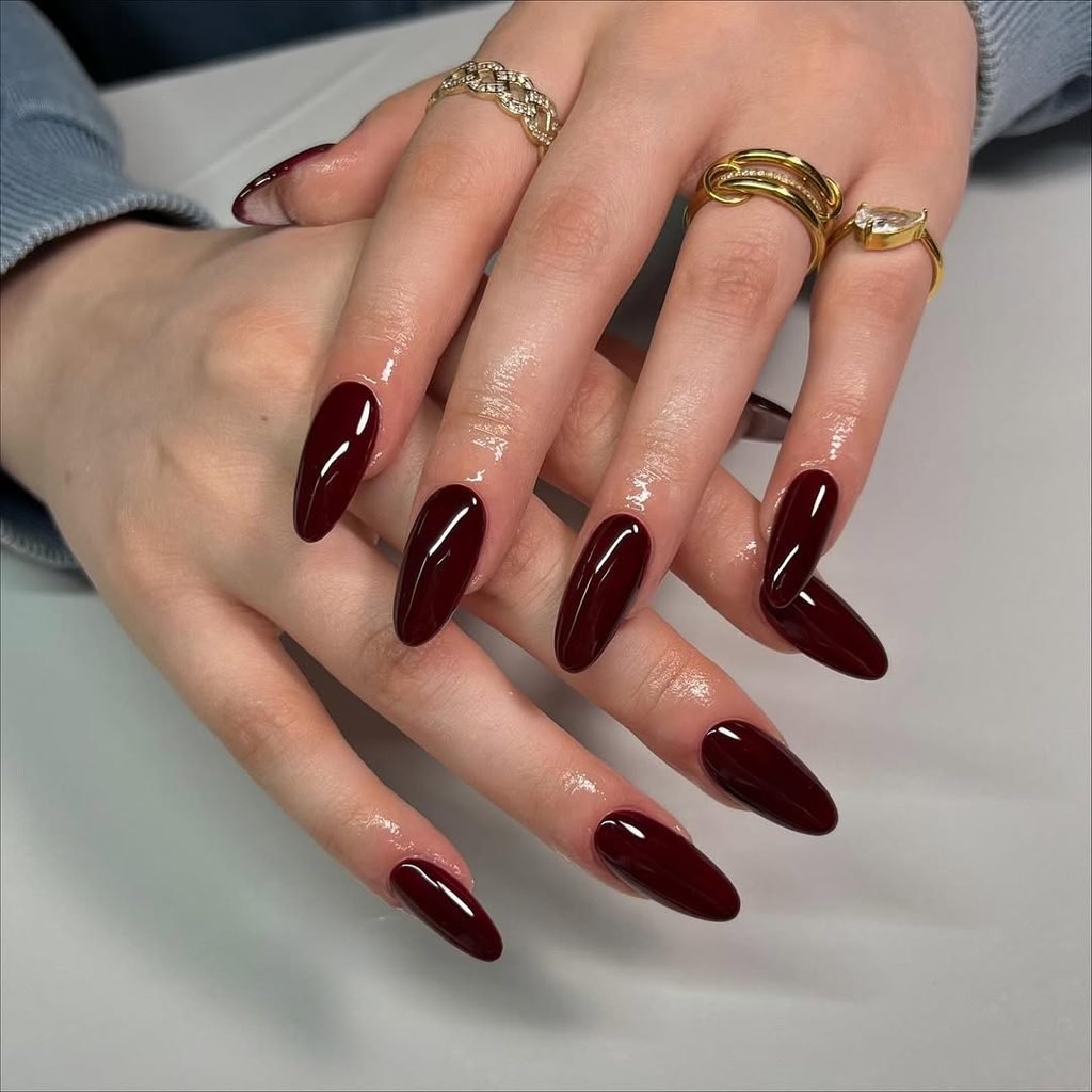 glossy deep burgundy wine red almond nails on hands wearing gold rings