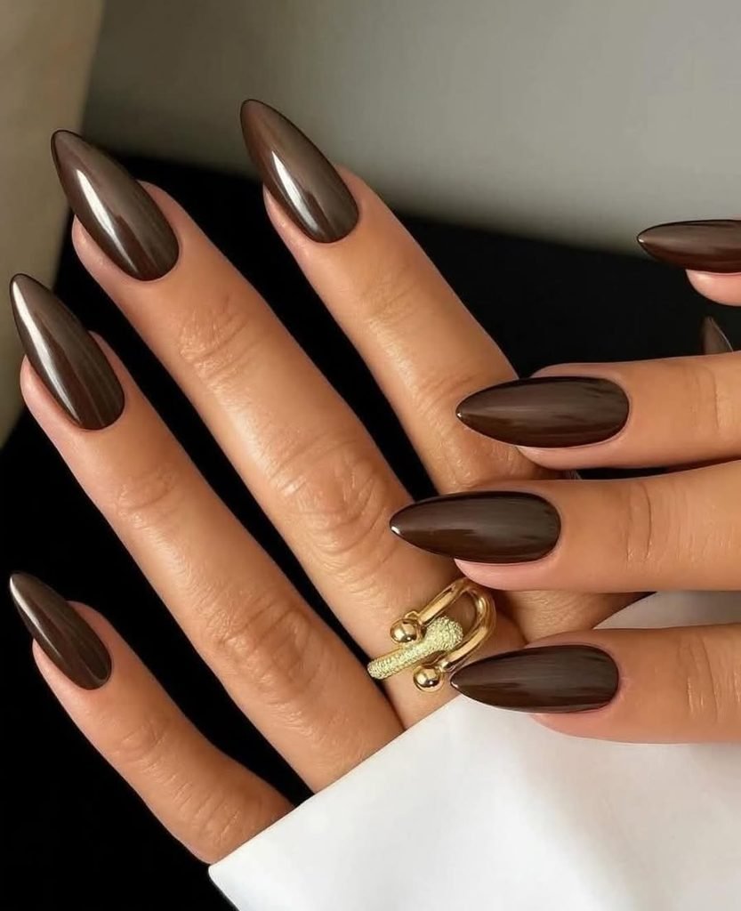 glossy dark chocolate brown almond shaped nails on a hand with gold ring