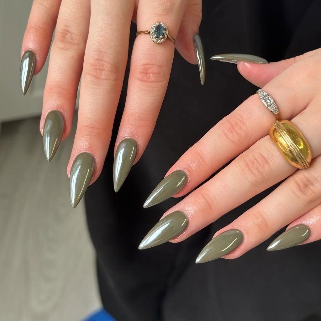 long olive green chrome stiletto nails on hands wearing gold rings