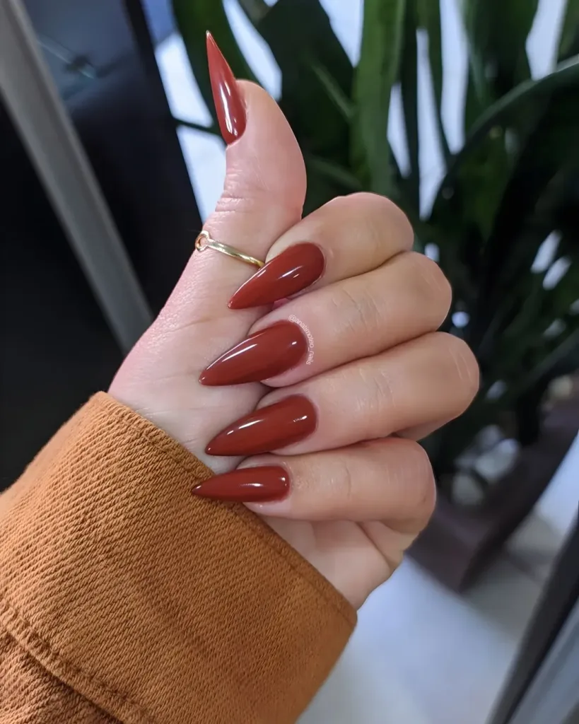 long burnt orange stiletto nails on a hand wearing a thin gold ring