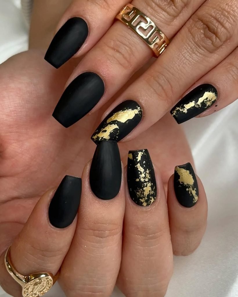 matte black coffin nails with gold foil accents and gold rings on fingers