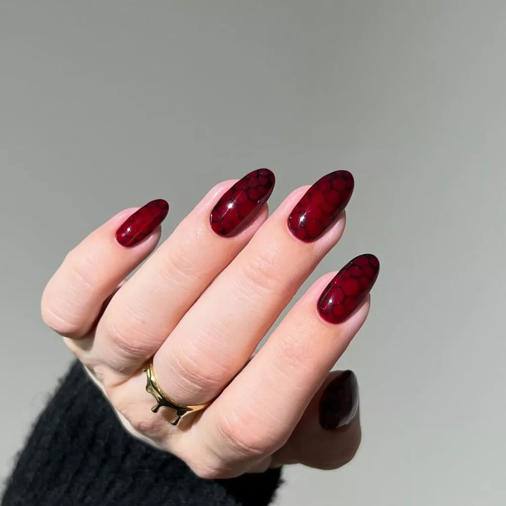 long oval shaped red and black patterned halloween nails on a hand with a gold ring