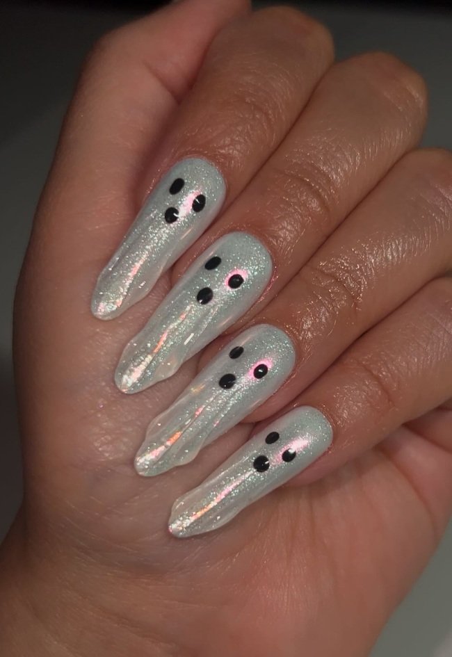 shimmering white iridescent ghost nails with black eyes and mouth details on a hand