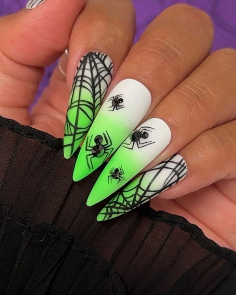 neon green and white ombre stiletto nails with black spiderwebs and rhinestones