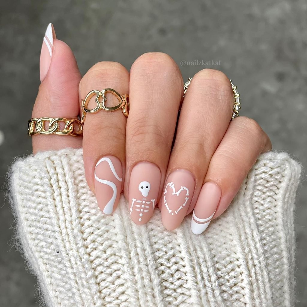 matte nude almond nails featuring white skeleton art and a heart made of bones