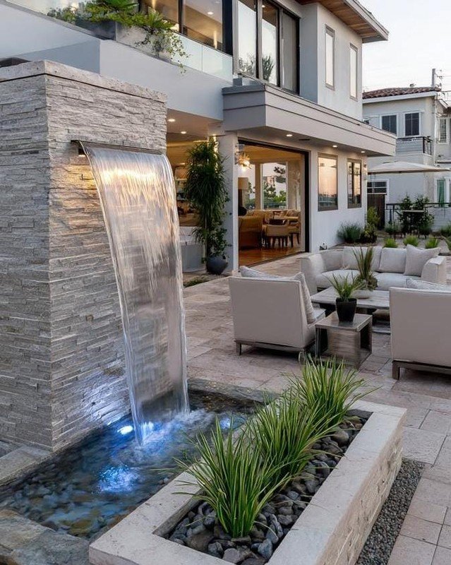 luxury stone patio featuring a modern sheet waterfall feature alongside contemporary outdoor seating