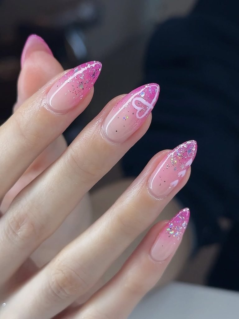 pink glitter ombre almond nails with white heart designs on a hand