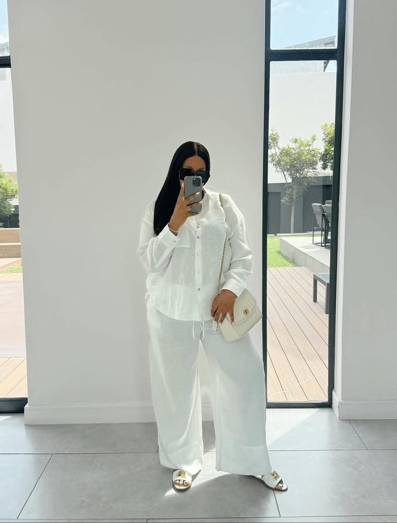 woman taking mirror selfie wearing white linen shirt, matching wide leg trousers, and sunglasses