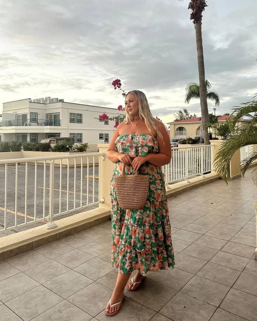 woman wearing a green floral strapless maxi dress and holding a woven tote bag