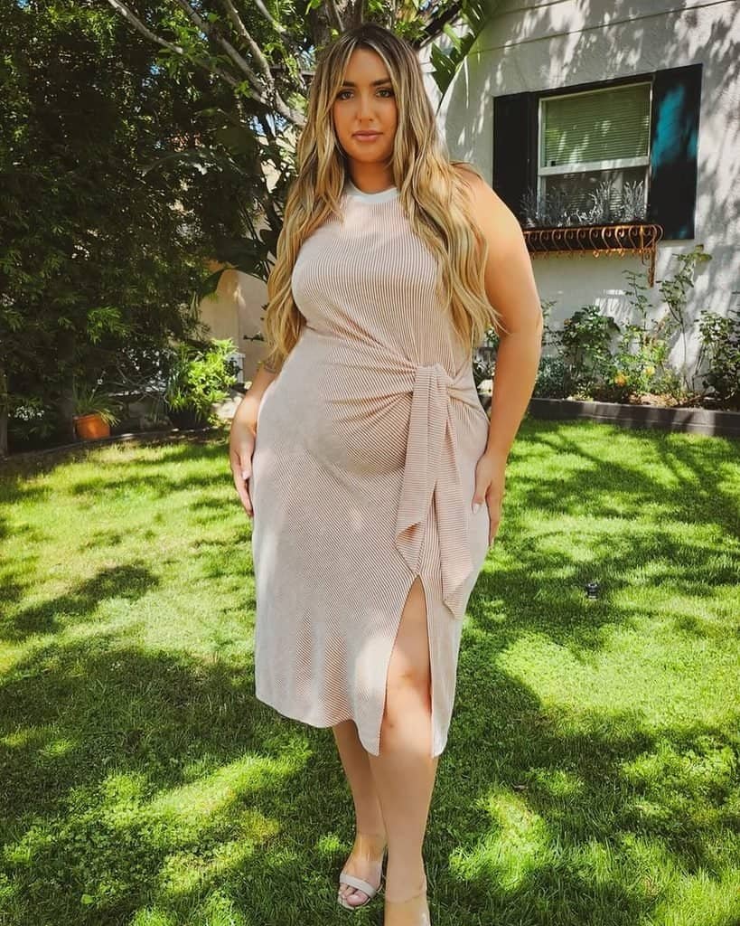 woman standing on a sunny lawn wearing a beige sleeveless wrap dress with a slit